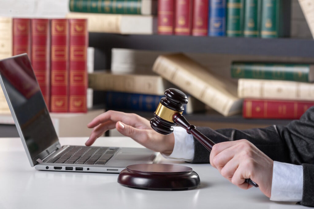 Woman in robes uses laptop with one hand and hammers gavel with other.