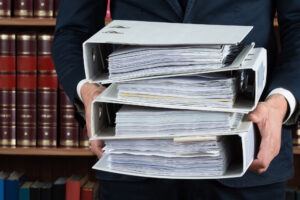 Midsection of male lawyer carrying stack of ring binders in courtroom